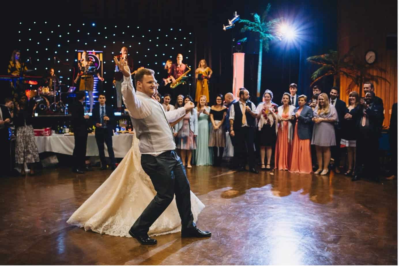 Groom dancing at wedding reception with live band and guests watching